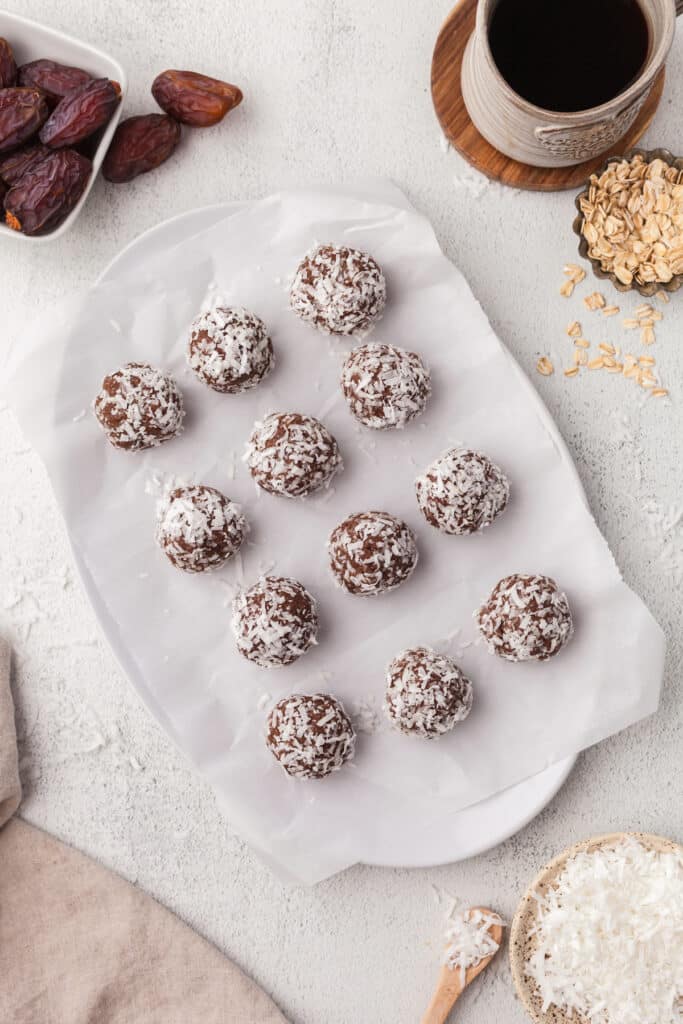 Coconut protein balls lined up on parchment paper after being rolled in coconut.