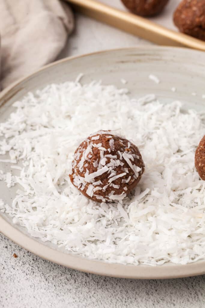 Coconut protein balls being coated in shredded coconut.