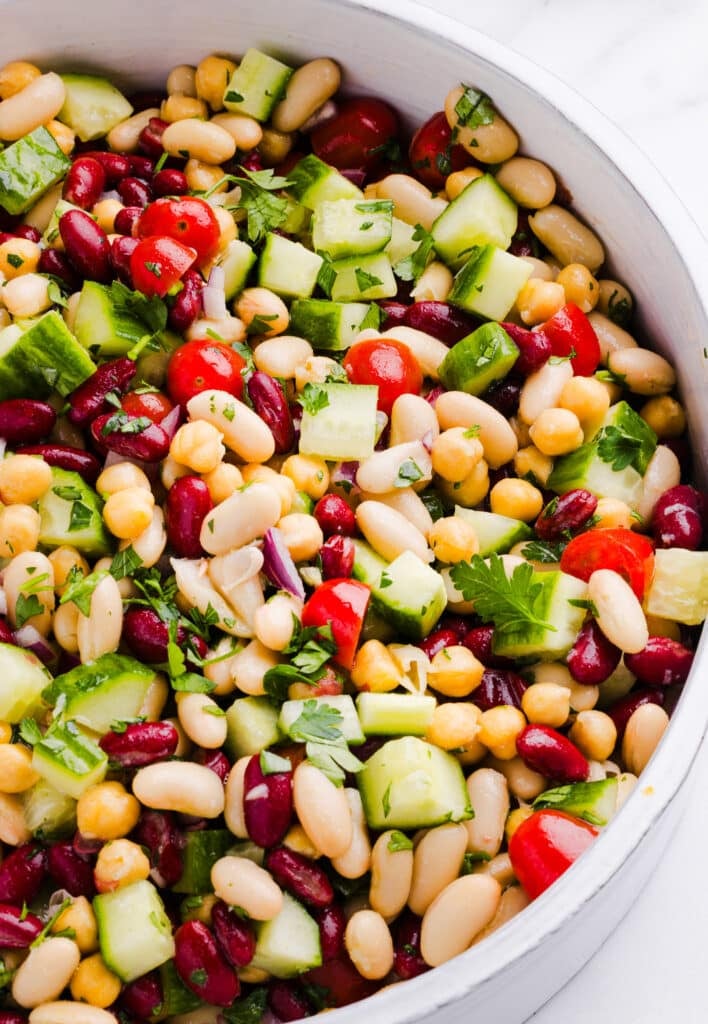 A close up shot of Italian bean salad with beans, cucumbers, tomatoes and parsley.