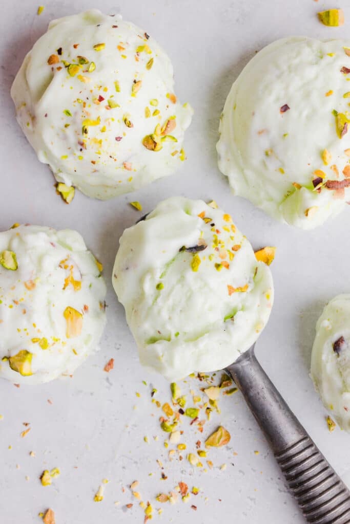 Scoops of pistachio ice cream on a countertop with spinkles of chopped pistachios.