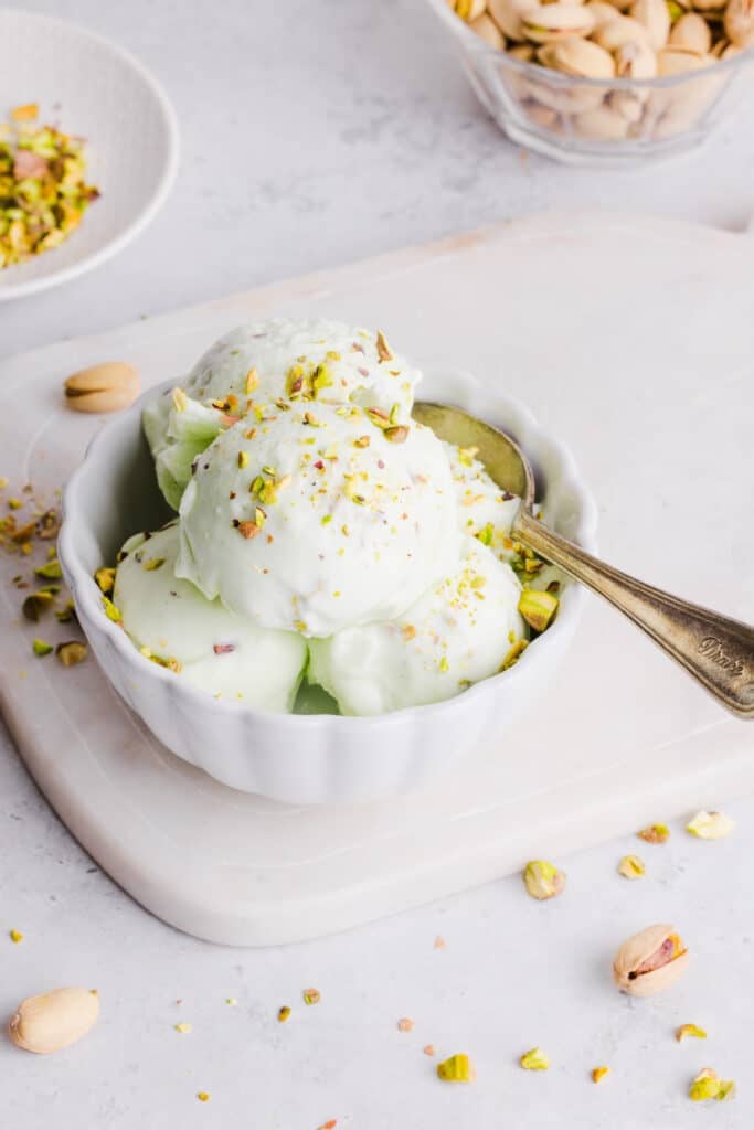 Ninja Creami pistachio ice cream in a bowl with pistachios sprinkled on top and a spoon.