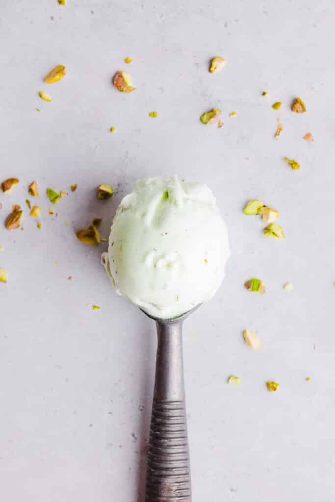 A single scoop of pistachio ice cream with pistachios sprinkled around it