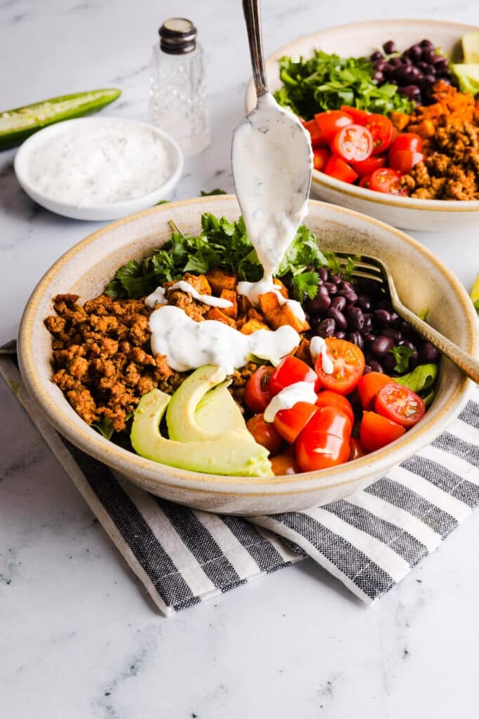 Garlic dressing being drizzled on top of a sweet potato taco bowl.