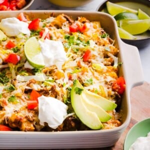 Taco potato casserole baked in a dish and topped with shredded lettuce, cheese, sour cream, avocado, lime and tomatoes.
