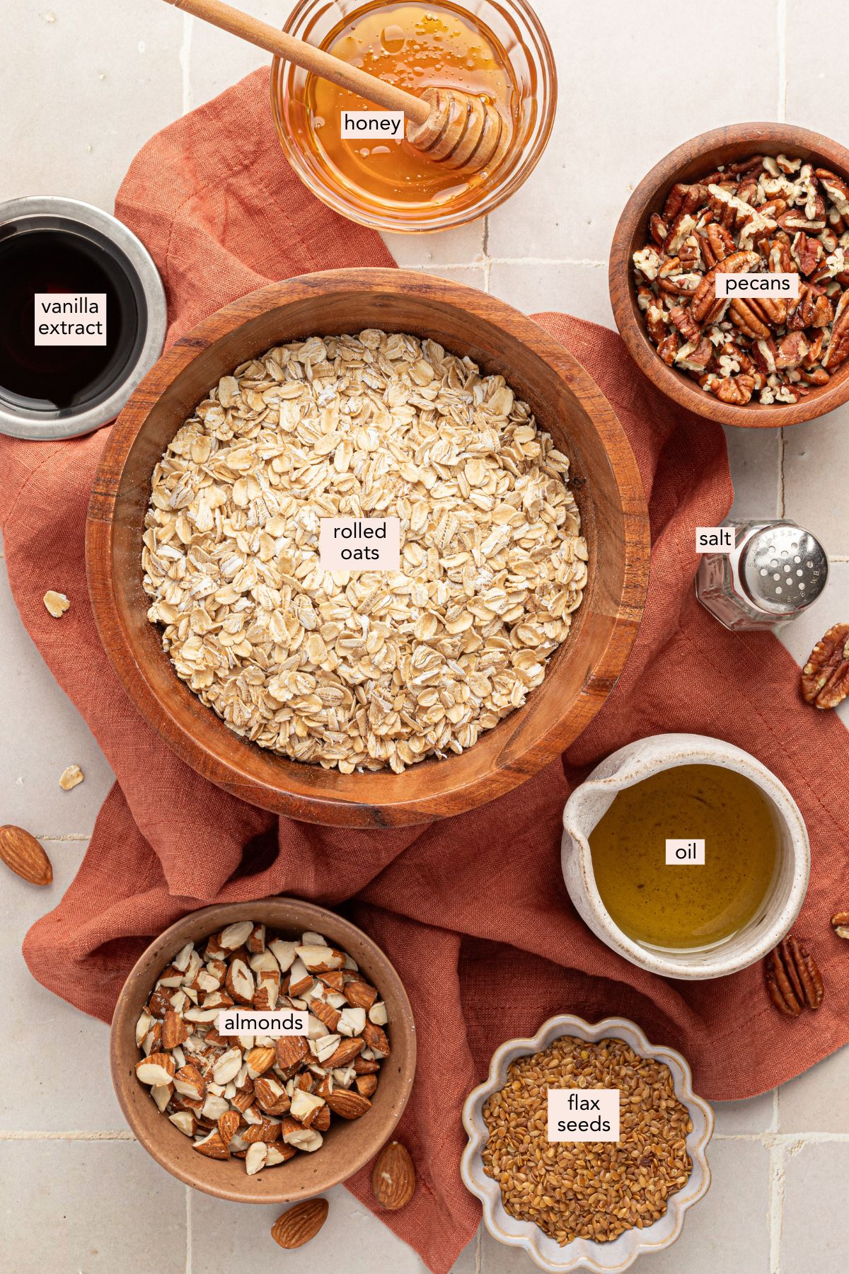 Ingredients for vanilla nut granola on a countertop with labels and a linen cloth.
