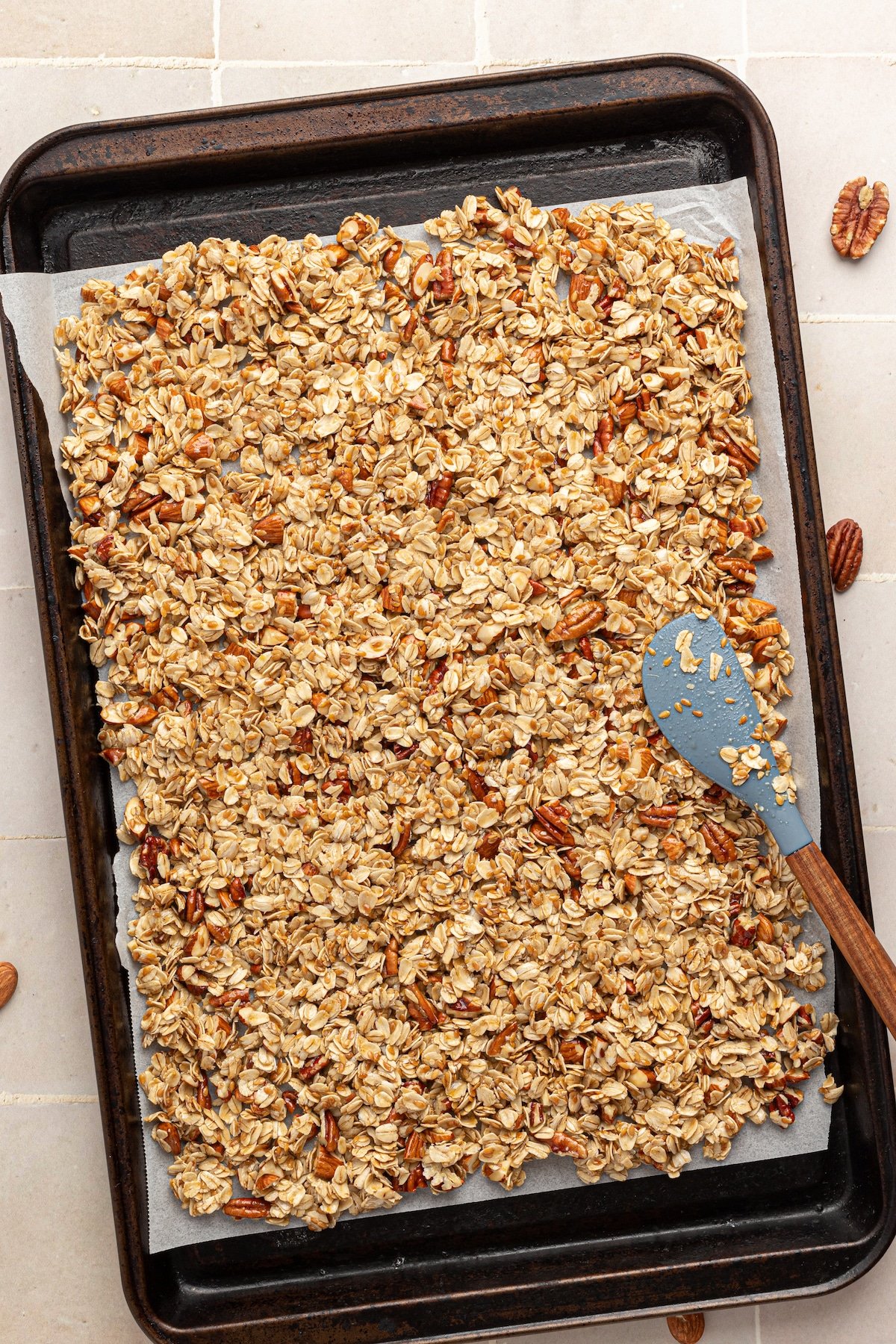 Vanilla nut granola being pressed onto a sheet pan with parchment paper.