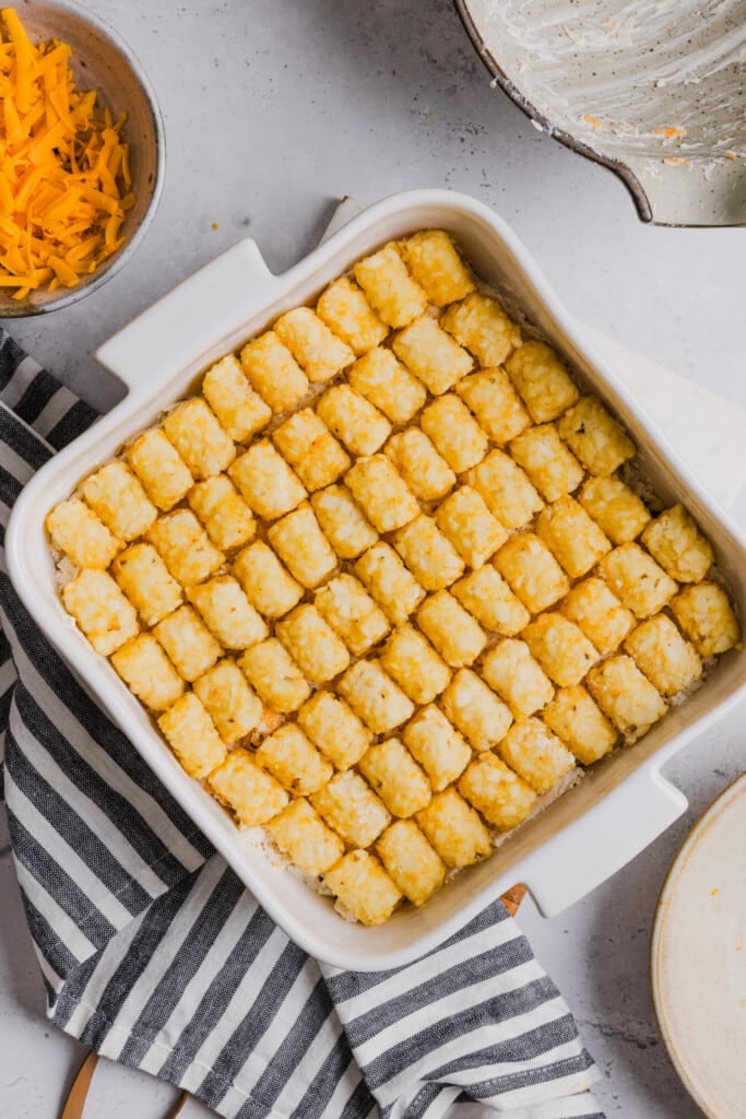 Chicken bacon ranch casserole with tater tots topped with frozen tater tots ready for the oven.