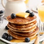 Protein pancakes without protein powder stacked on a plate with maple syrup, butter and blueberries.