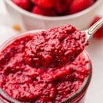 A spoon lifting some raspberry chia jam out of a jar.
