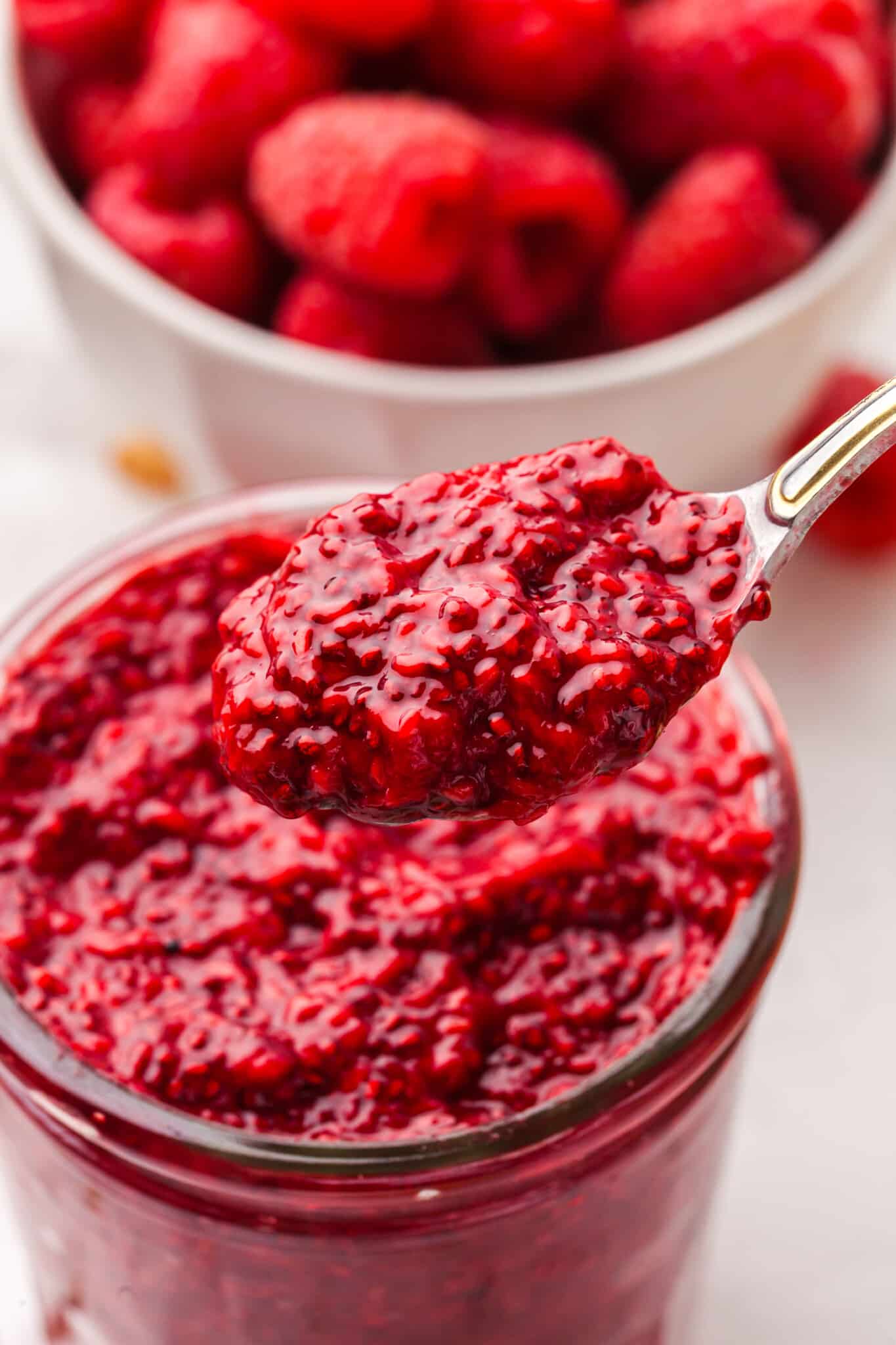This 15-minute Raspberry Chia Jam made with raspberries, lemon juice, chia seeds, and honey is loaded with flavor, fiber, and antioxidants. A spoon lifting some raspberry chia jam out of a jar.