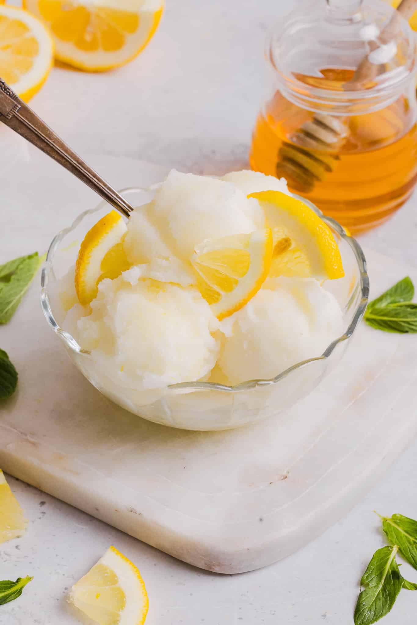 A bowl of lemon sorbet next to a ja of honey.