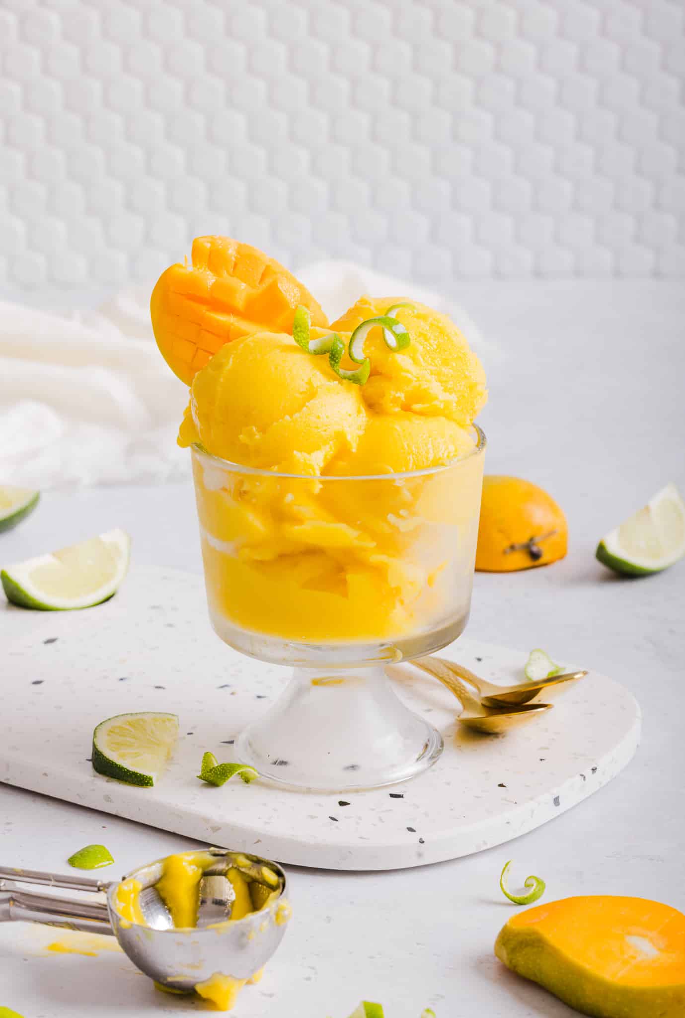 This 3-ingredient Ninja Creami mango sorbet is thick, creamy, and free of added sugars! Fresh mango and lime juice make a refreshing treat. Mango garnishes a dish of manjo sorbet.