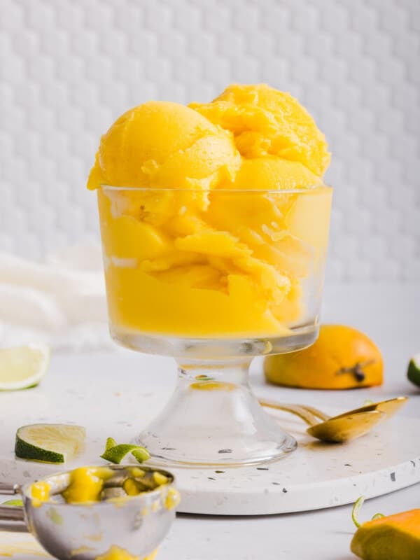 Bright orange scoops of mango sorbet in a glass dish.
