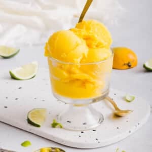 Scoops of Ninja Creami mango sorbet served in a glass dish with a spoon.