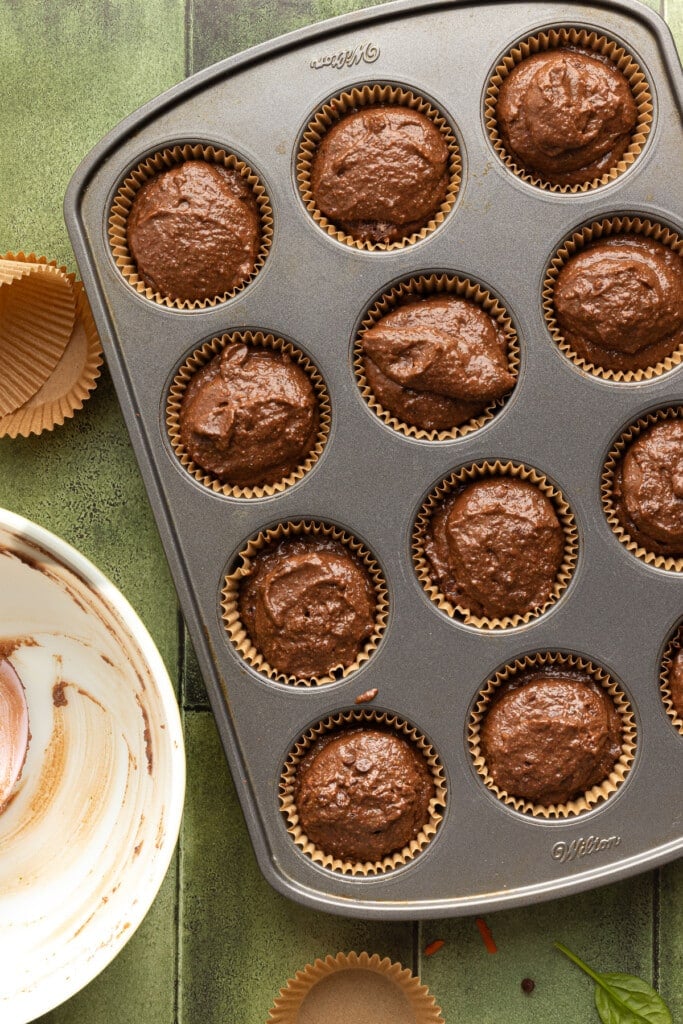 Chocolate veggie muffin batter being scooped in a muffin pan with liners.