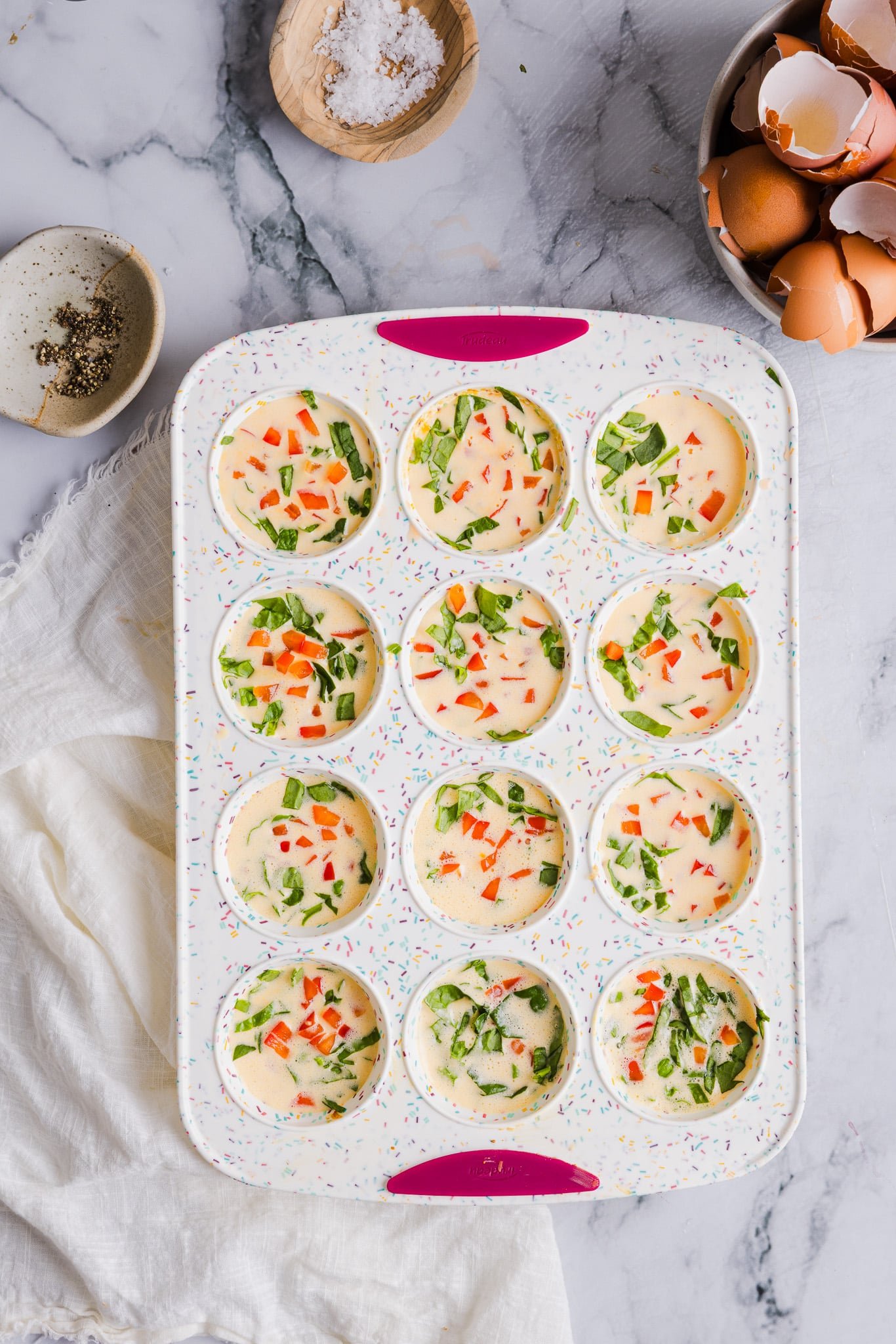 Veggies added to a cottage cheese egg mixture in a silicone muffin pan.