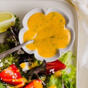 Mango vinaigrette in a scalloped bowl next to a strawberry salad