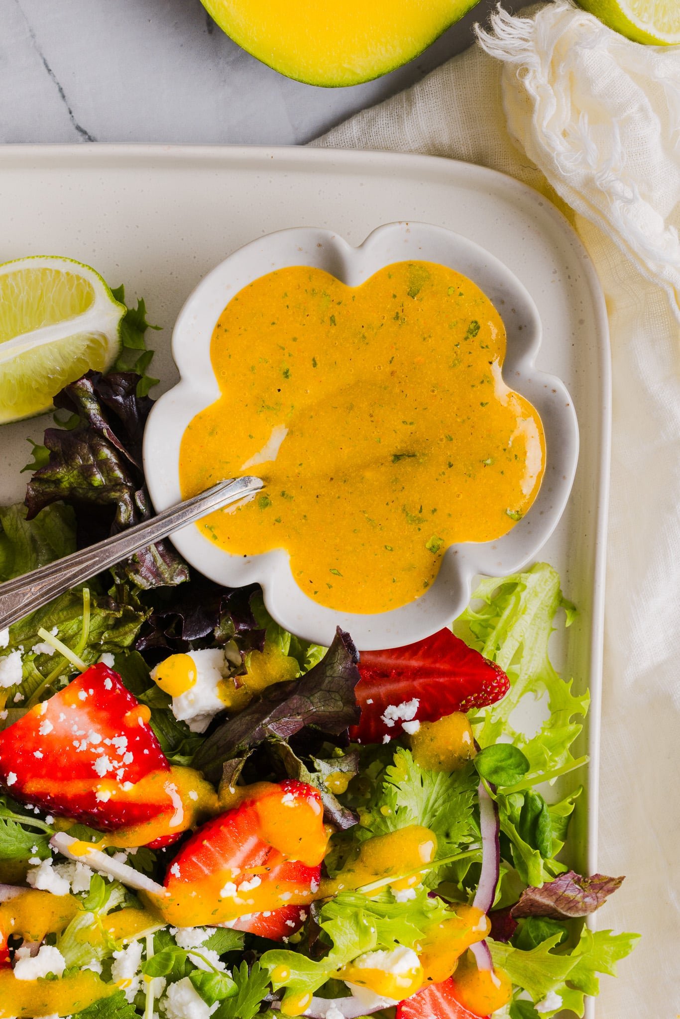 Mango vinaigrette in a scalloped bowl next to a strawberry salad.