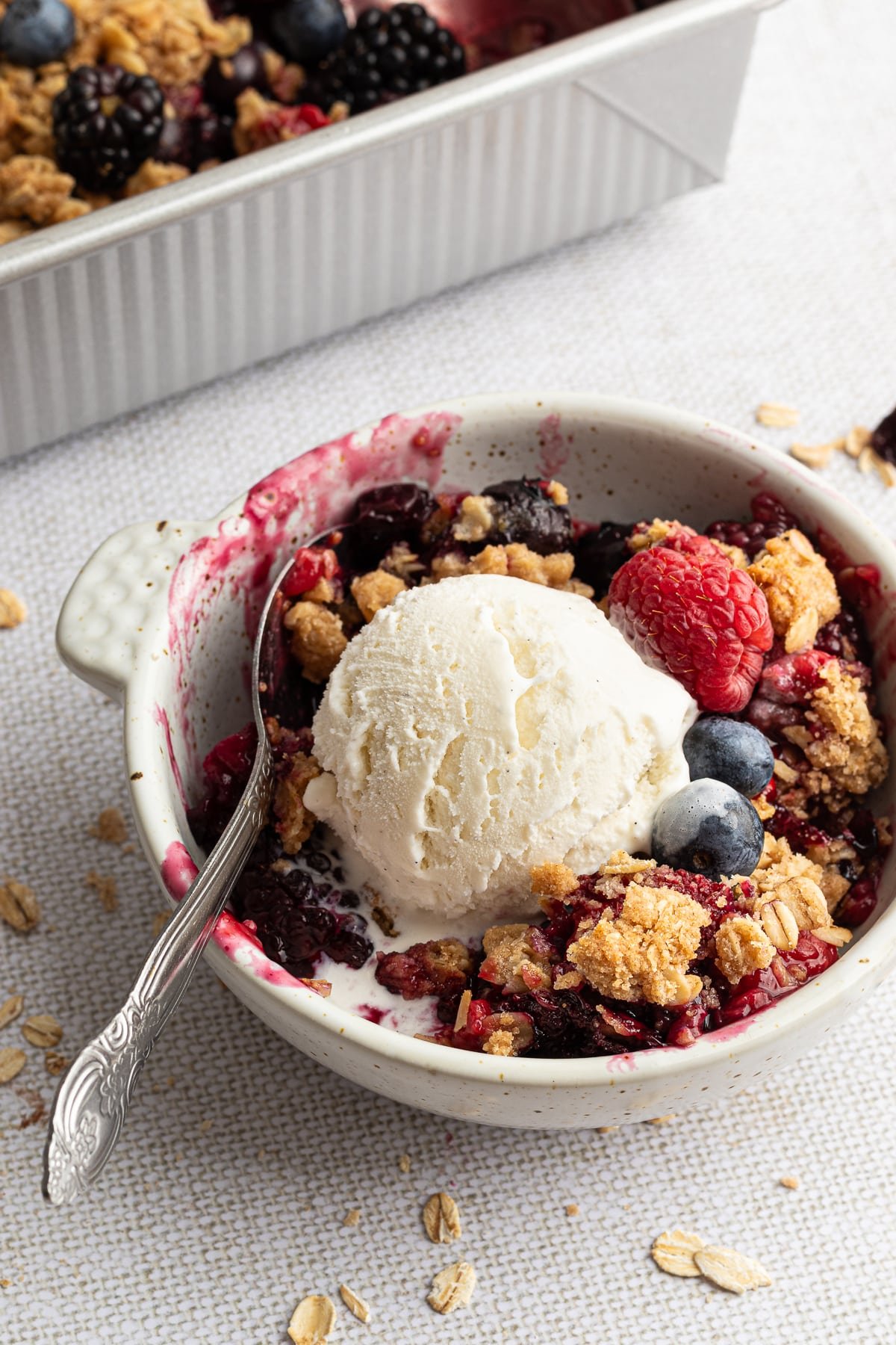 This berry crumble recipe is to die for. Honey-sweetened berries and a buttery, cinnamon topping come together in the perfect summer treat. A serving of berry crumble topped with a scoop of vanilla ice cream.
