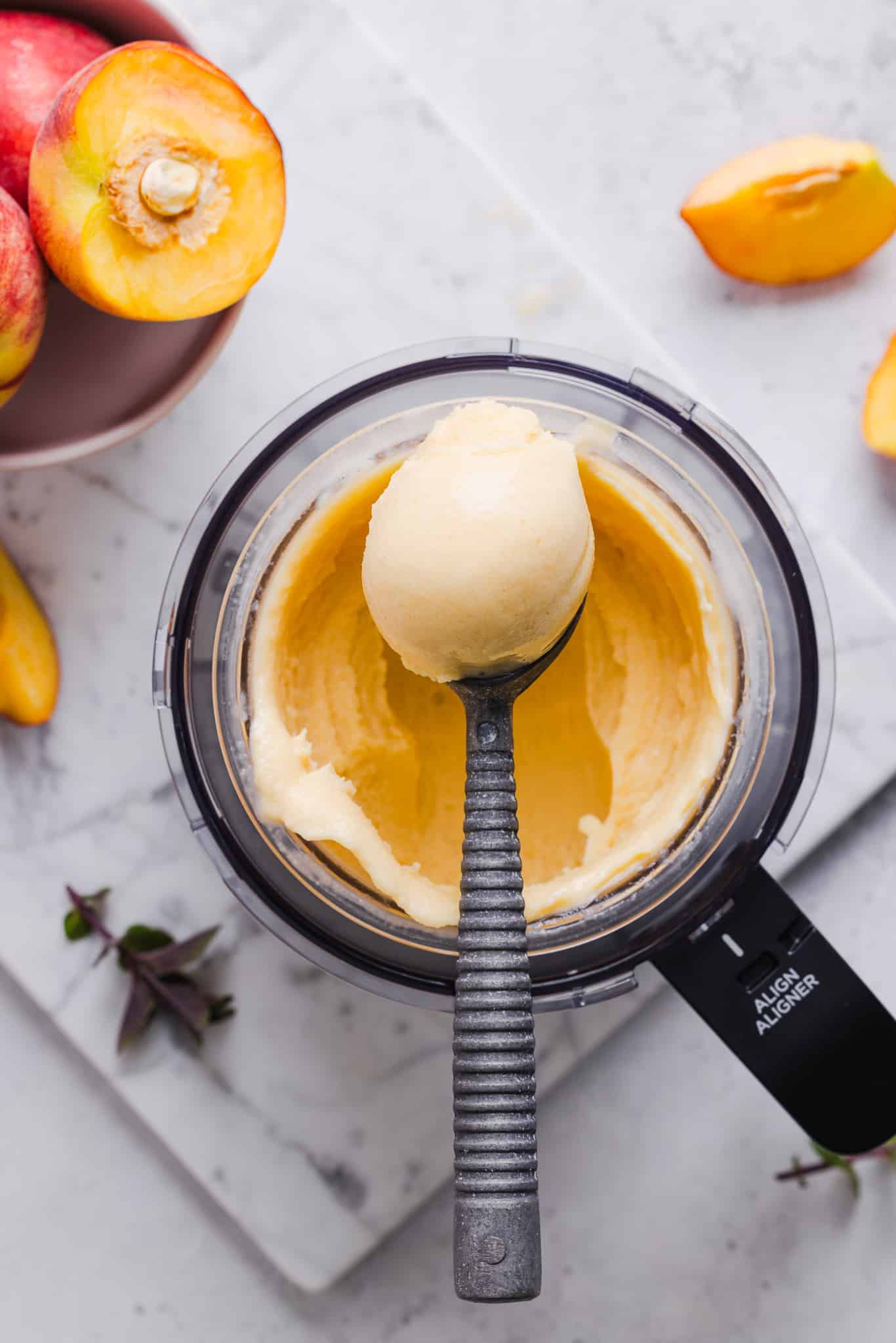 Scooping peach ice cream out of a Ninja Creami machine.
