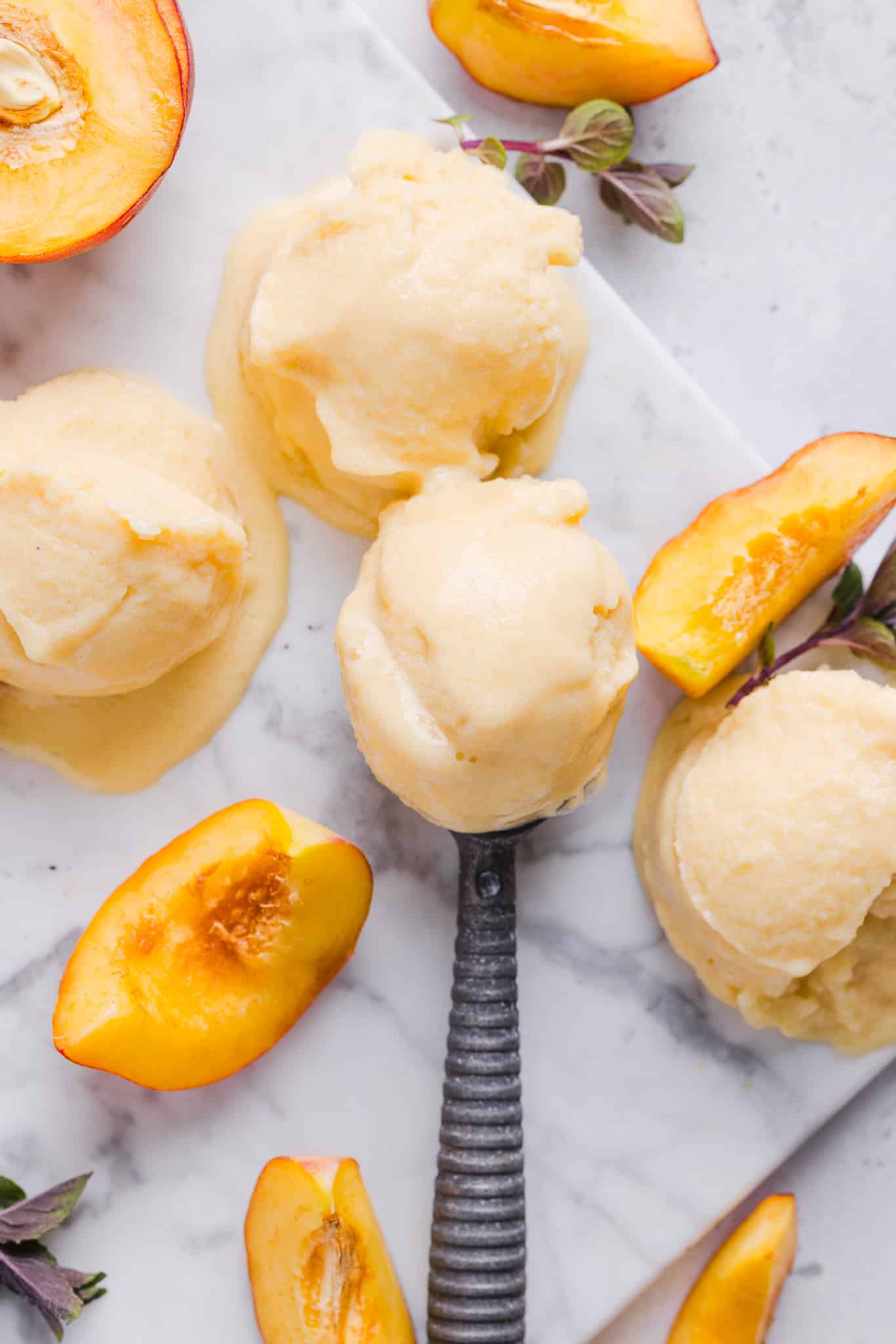 Scoops of Ninja Creami peach ice cream on a work surface with peach slices.