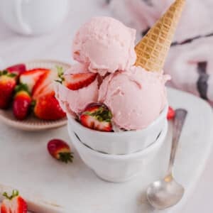 Scoops of strawberry ice cream in a bowl with a sugar cone.