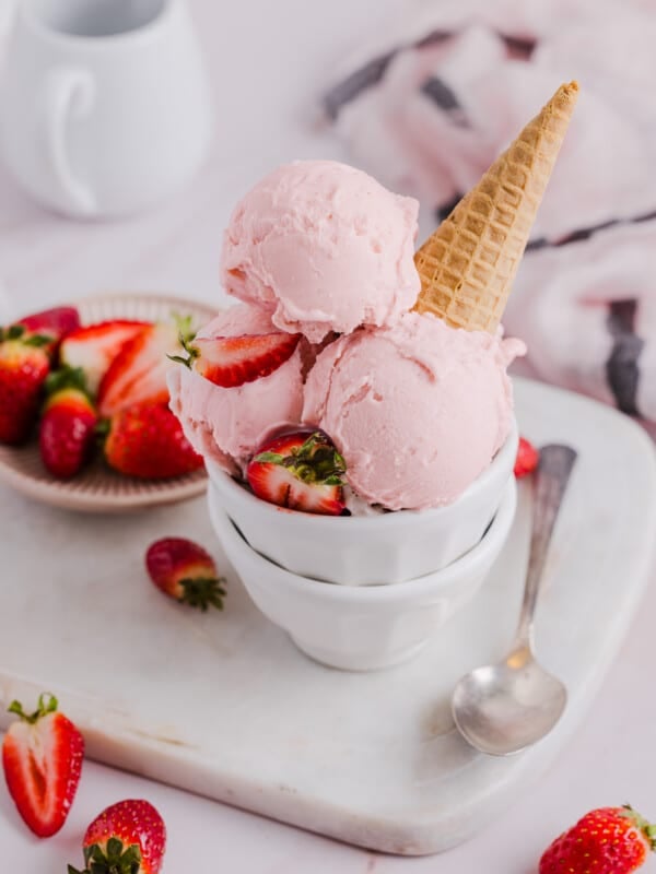 Scoops of strawberry ice cream in a bowl with a sugar cone.