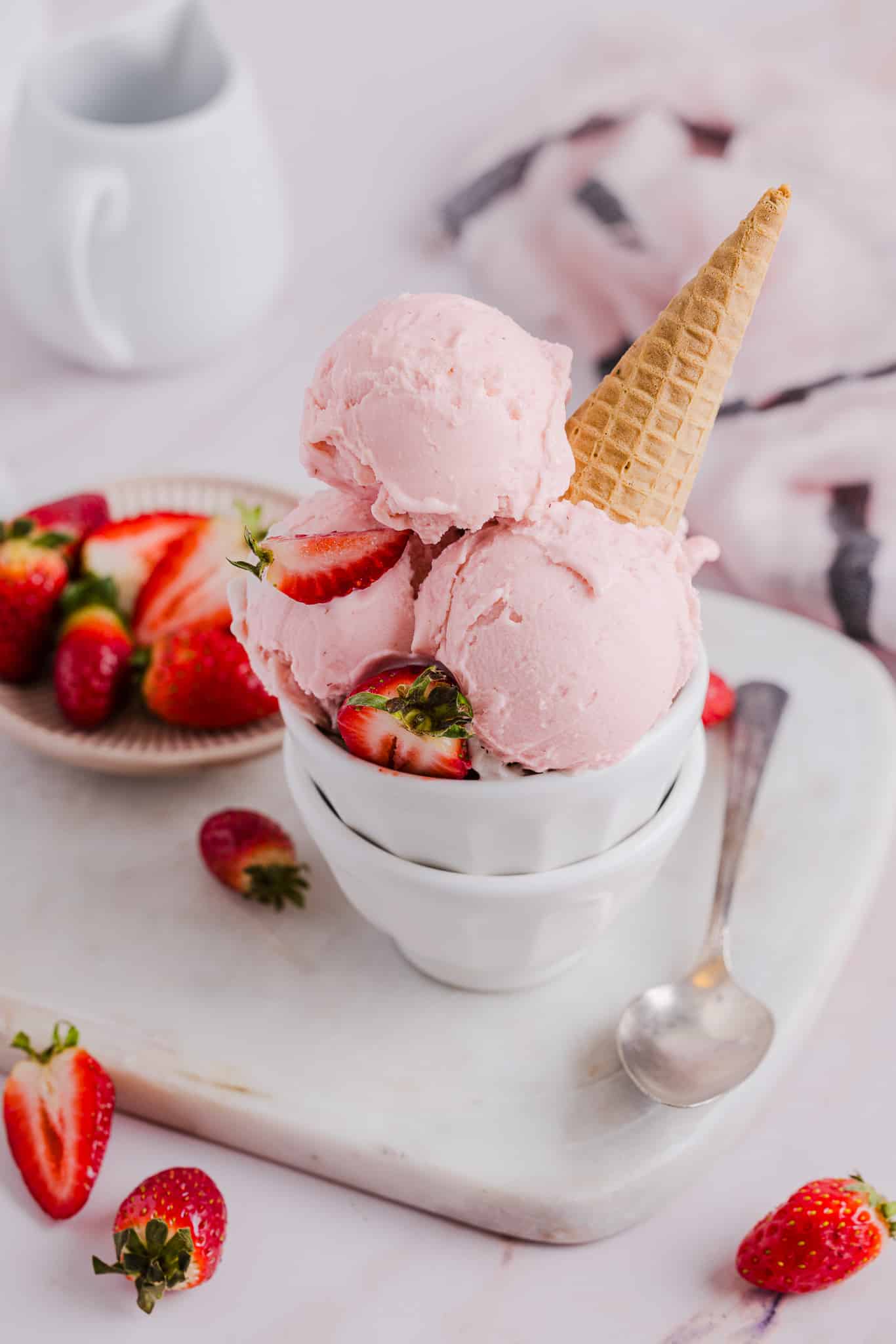This easy Ninja Creami Strawberry Ice Cream recipe blends juicy strawberries with a splash of cream for a perfectly refreshing summer treat. Scoops of strawberry ice cream in a bowl with a sugar cone.