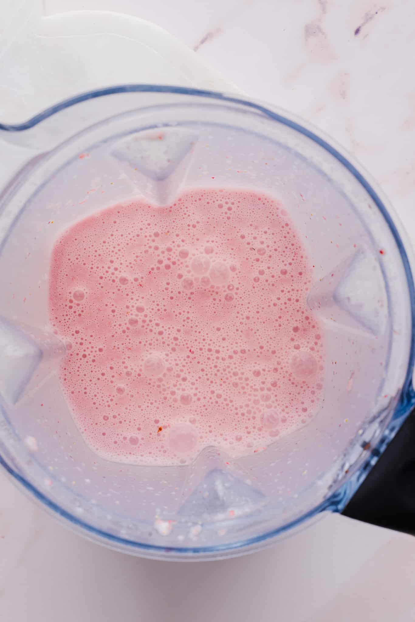 Ingredients for strawberry ice cream blended together in a blender.