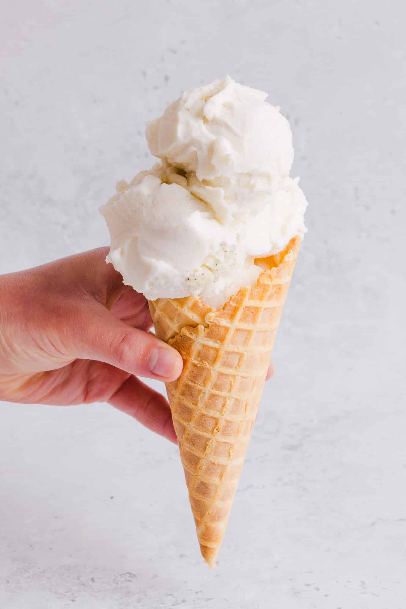 A hand holding an ice cream cone loaded with vanilla ice cream.