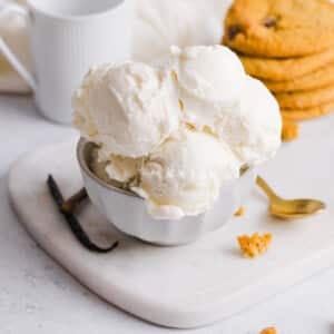 Scoops of vanilla ice cream in a bowl near a stack of cookies.