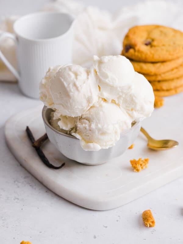 Scoops of vanilla ice cream in a bowl near a stack of cookies.