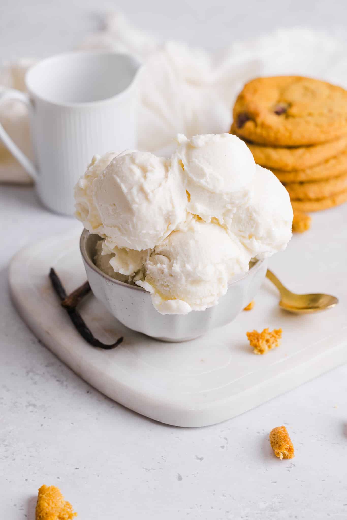 This Ninja Creami vanilla ice cream is incredibly rich and creamy! It delivers the luxury of premium ice cream without the guilt. Scoops of vanilla ice cream in a bowl near a stack of cookies.