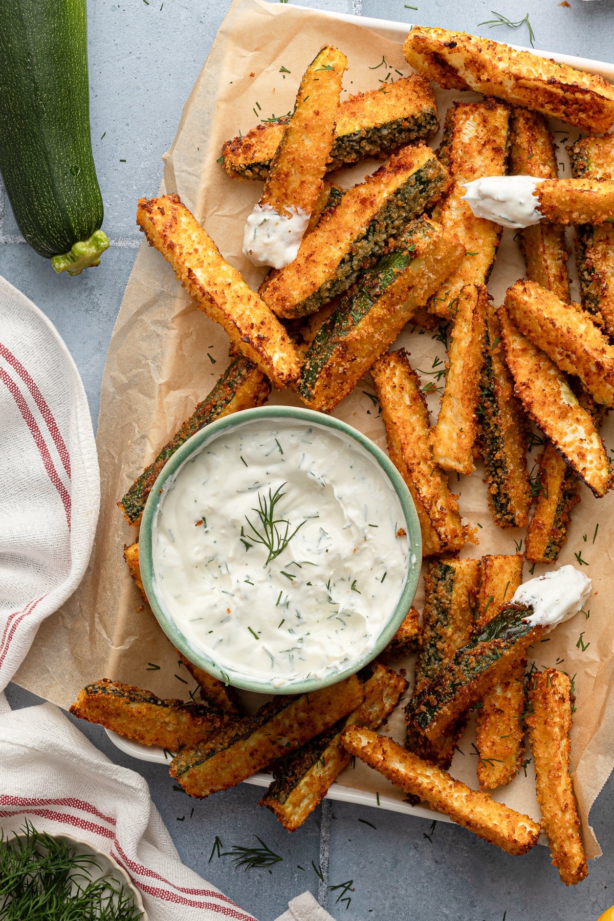Air fryer zucchini fries on parchment paper. Some are dipped in Greek yogurt dill sauce.