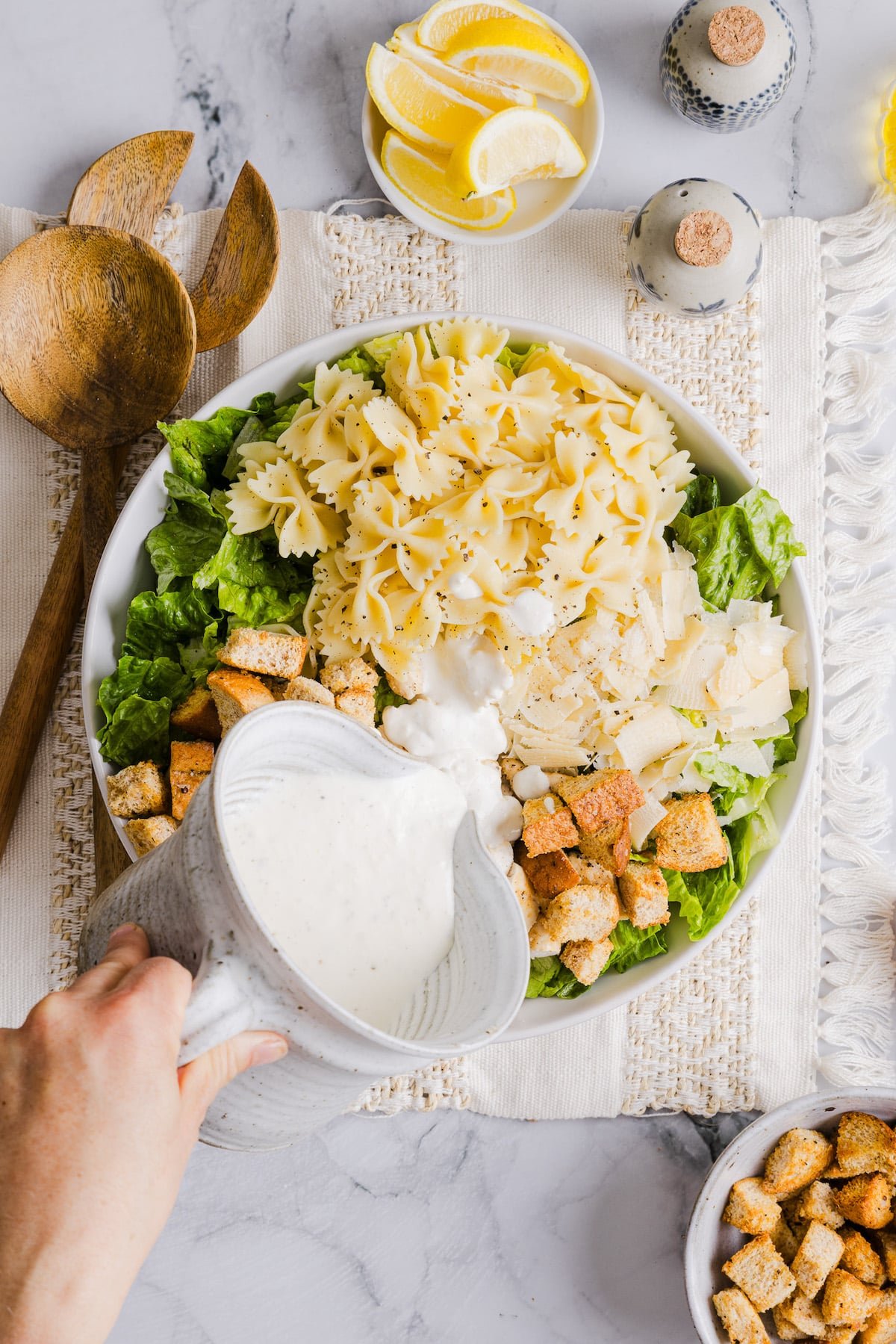 Caesar salad dressing being poured onto chicken caesar pasta salad.