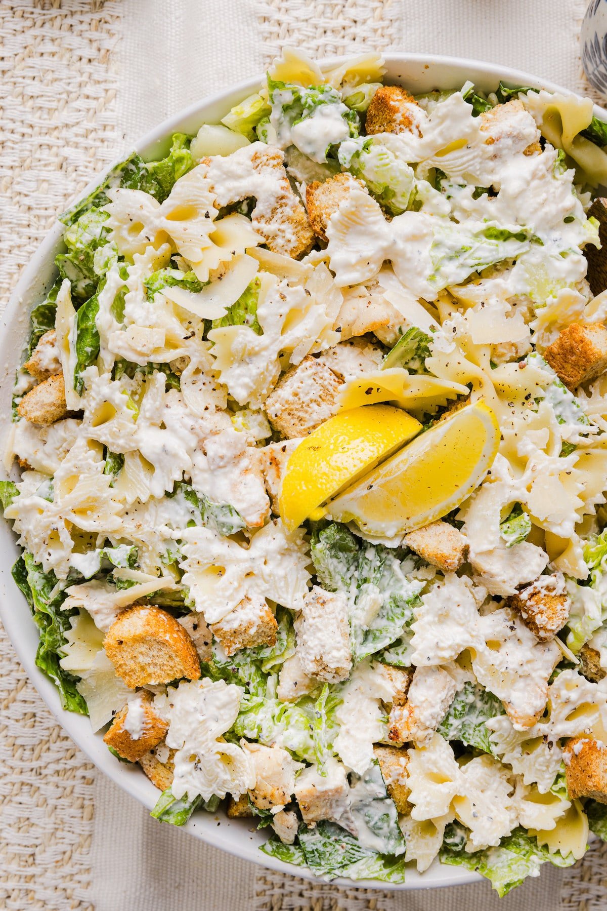 Chicken caesar pasta salad in a large bowl garnished with lemon.
