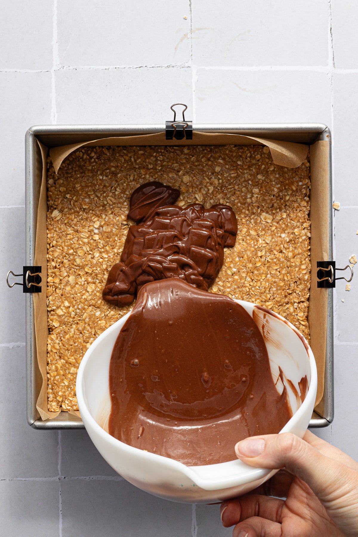 Melted chocolate and peanut butter being poured onto the oat layer for no bake chocolate oat bars.