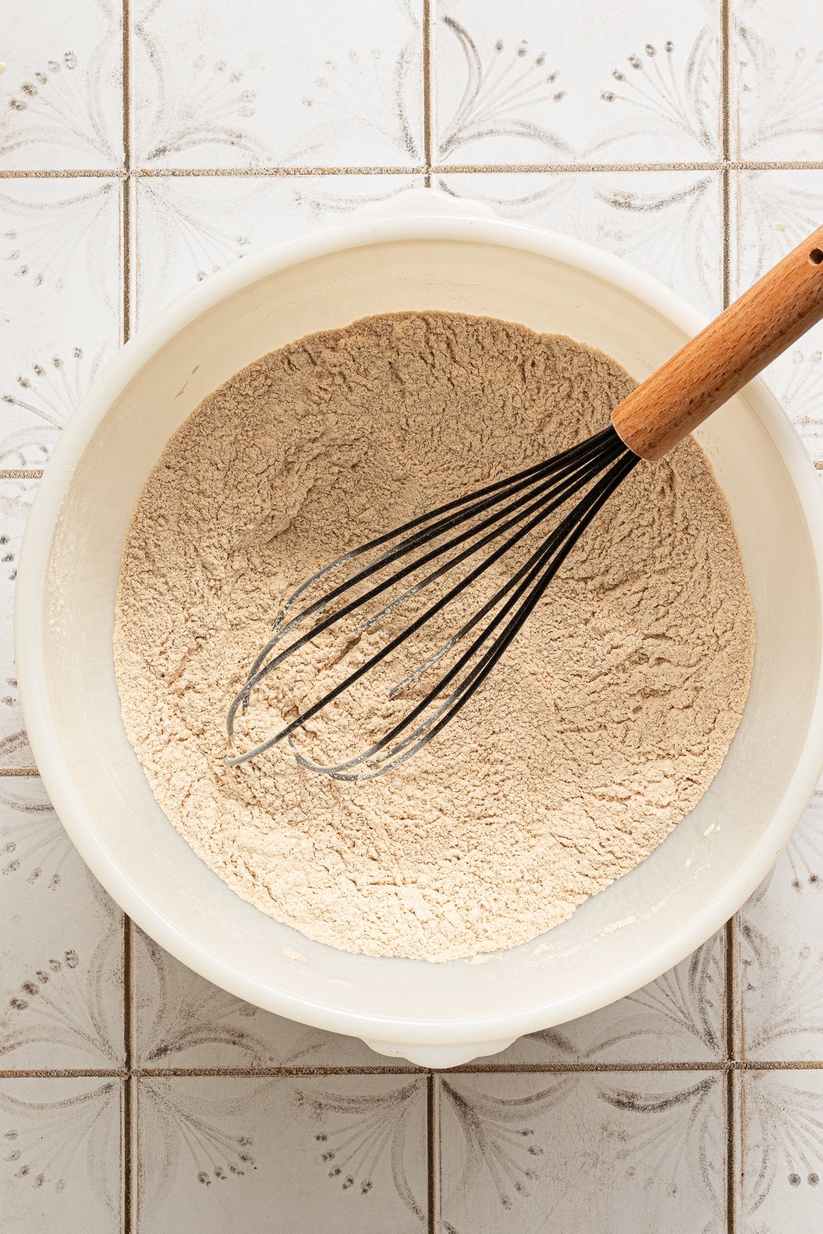 Dry ingredients for healthy chocolate zucchini bread mixed in a white bowl with a whisk.