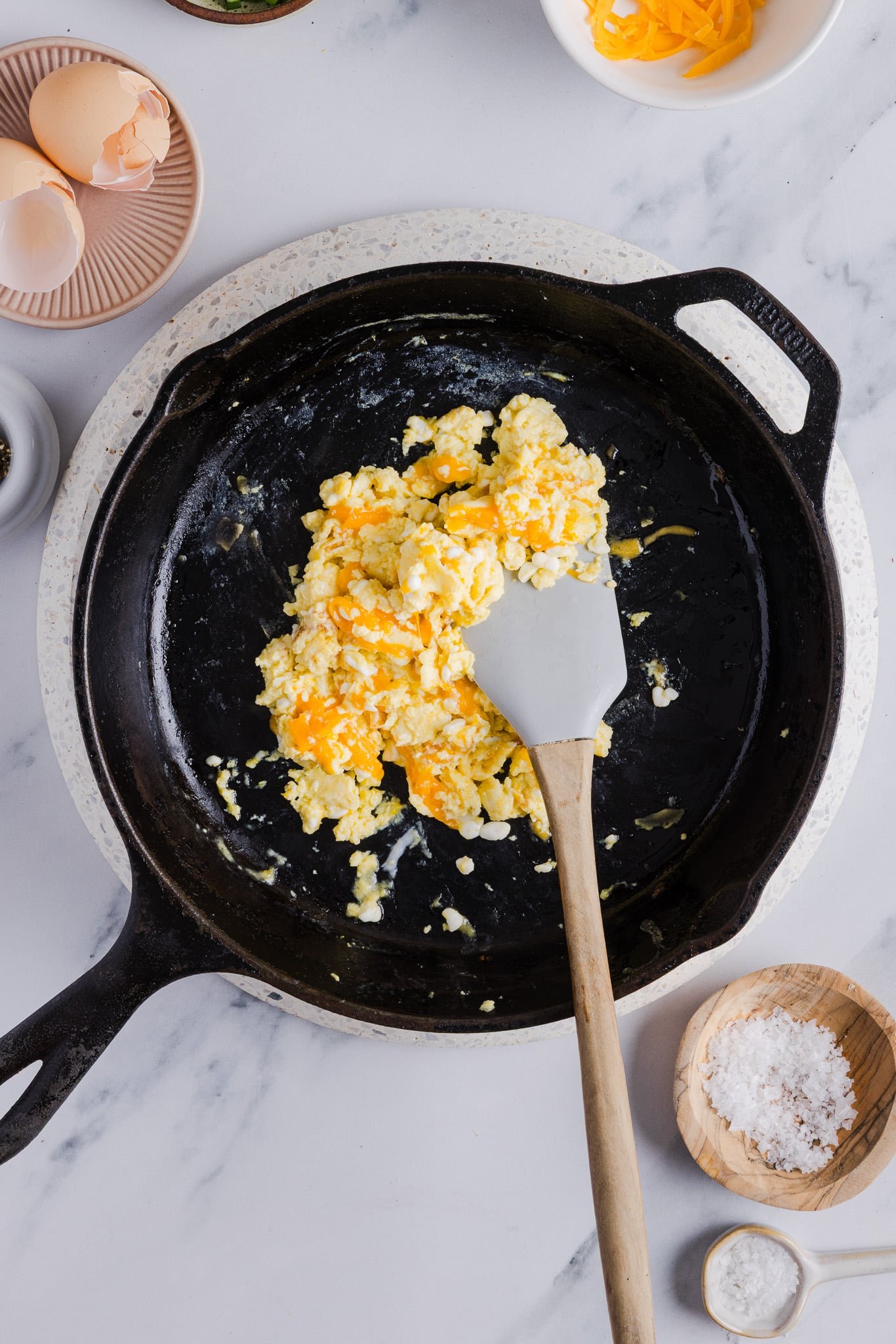 Cheddar cheese being added to cottage cheese eggs in a pan.