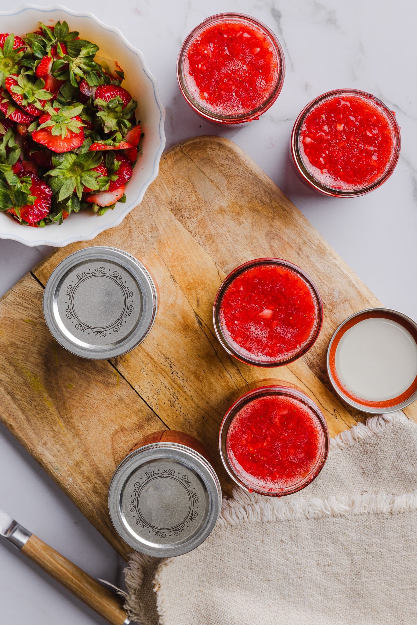Low sugar strawberry freezer jam in jars on a wooden board.