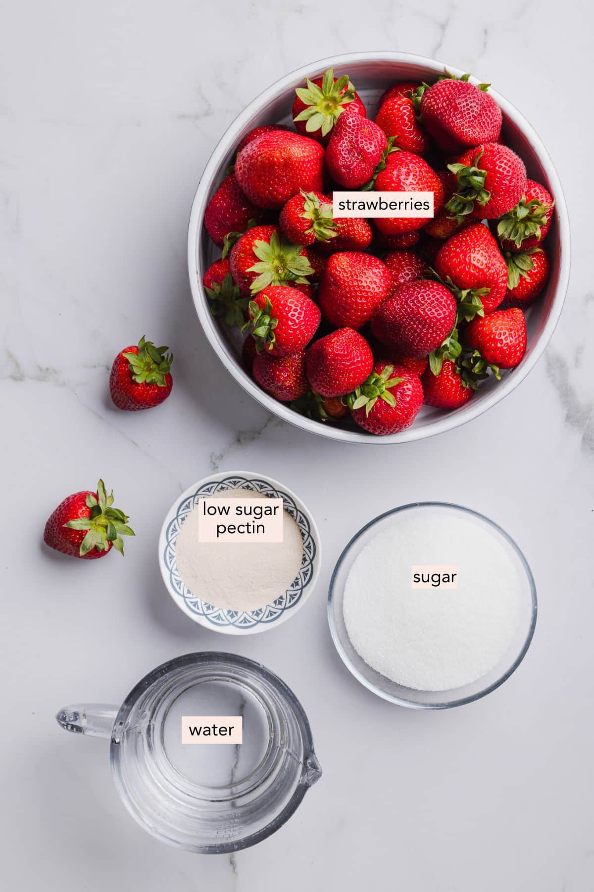 Ingredients for low sugar strawberry jam on a countertop with labels.