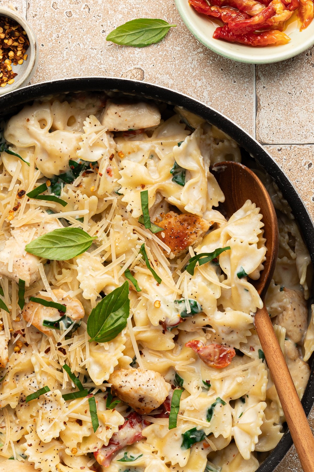 A close up shot of marry me chicken pasta in a pan with a wooden spoon.