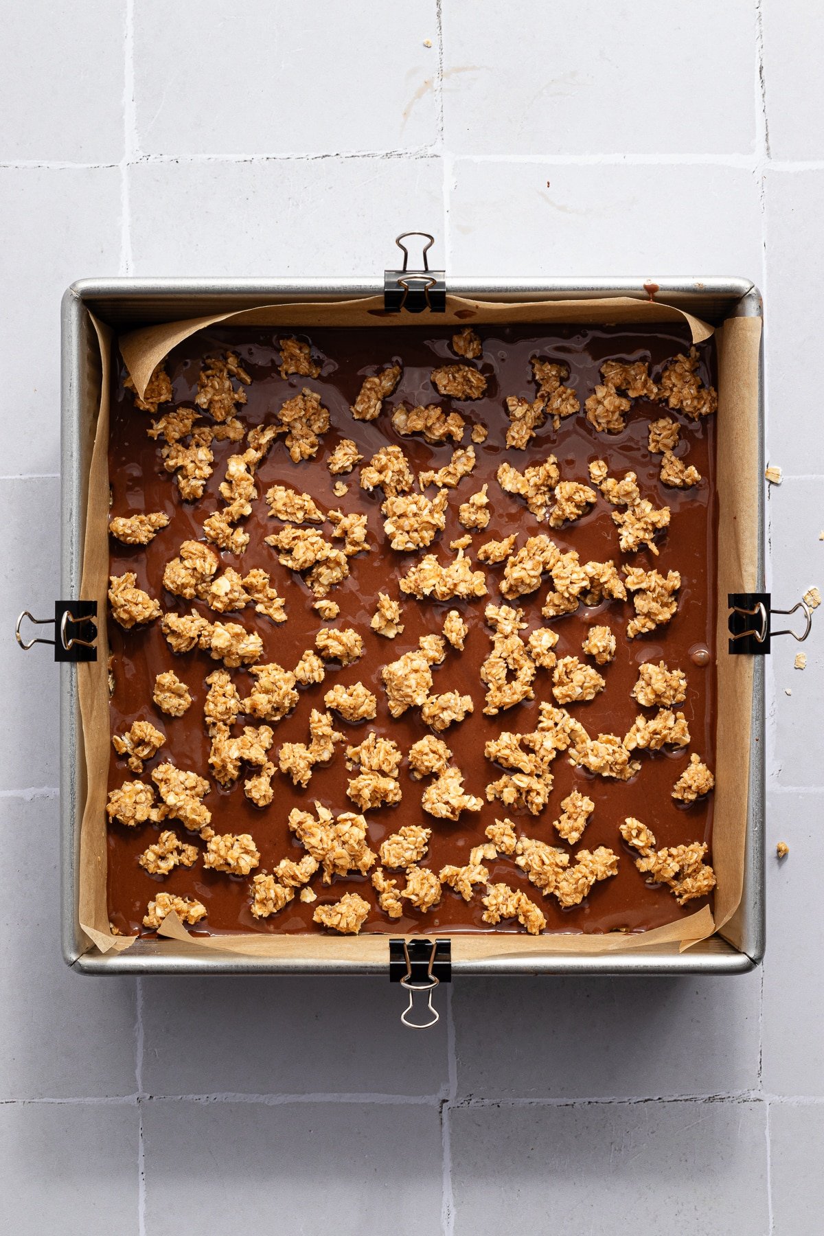 Crumbled oat mixture being added to the top of the chocolate peanut butter layer for no bake chocolate oat bars.