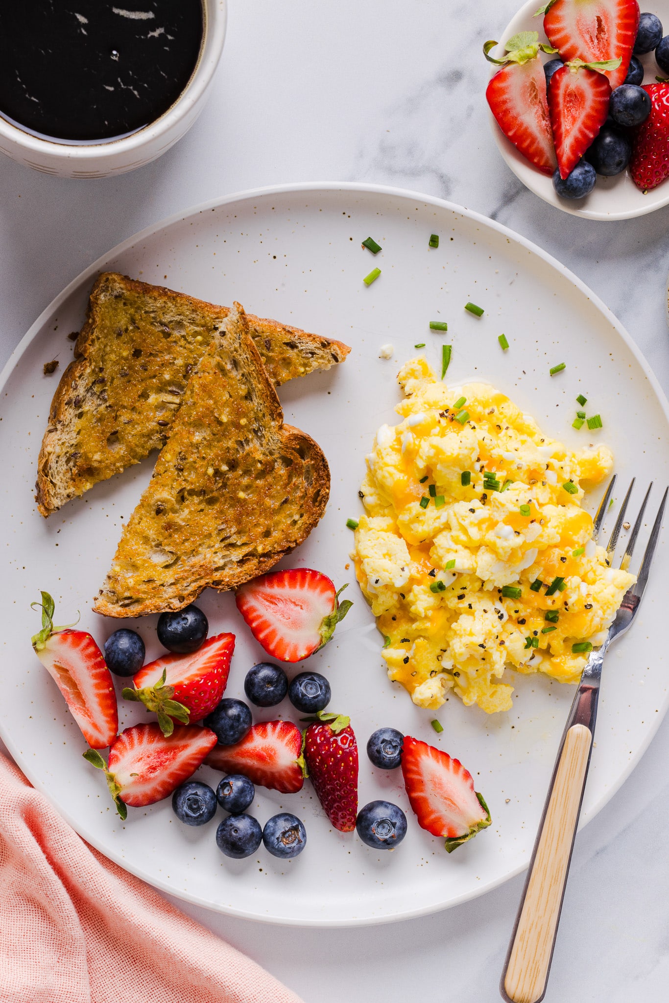 Cottage cheese eggs garnished with chives on a white plate with berries and toast.