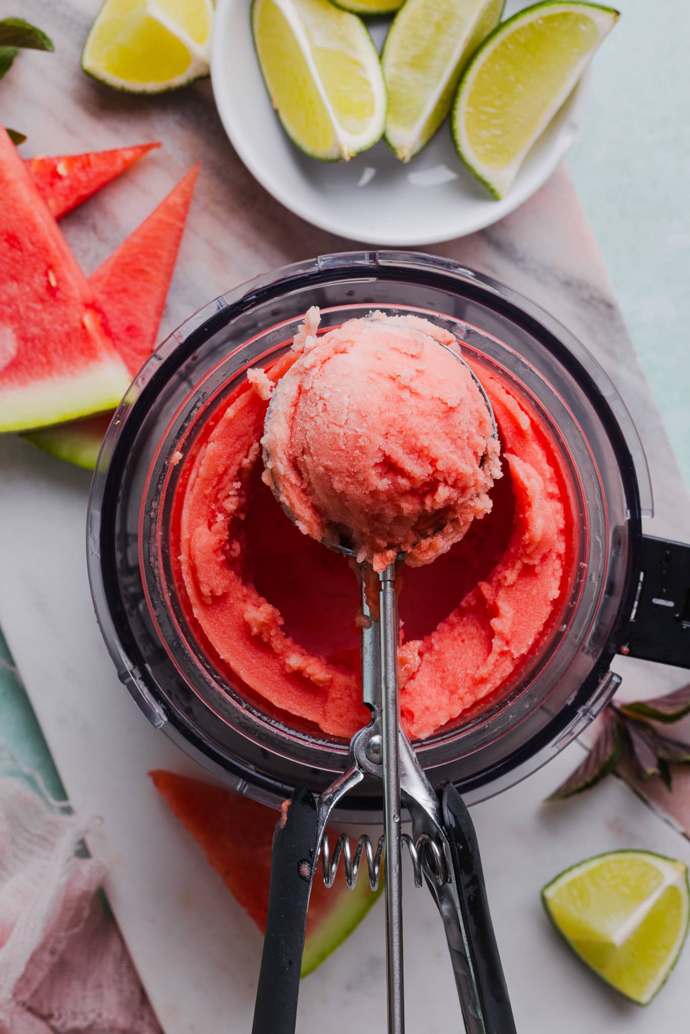 An ice cream scoop taking a scoop of watermelon sorbet from a Ninja Creami machine.