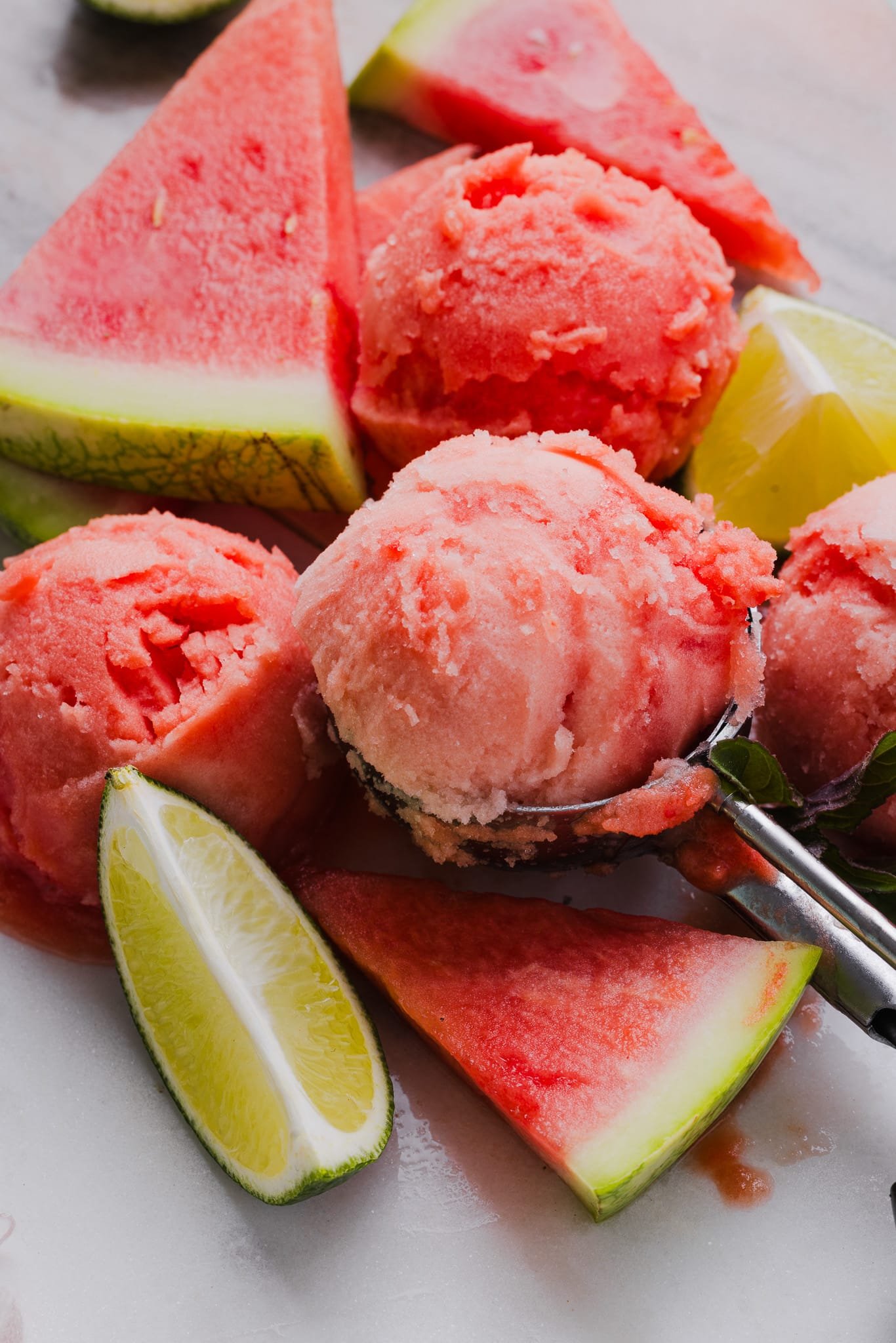 Scoops of watermelon sorbet with slices of watermelon and lime.
