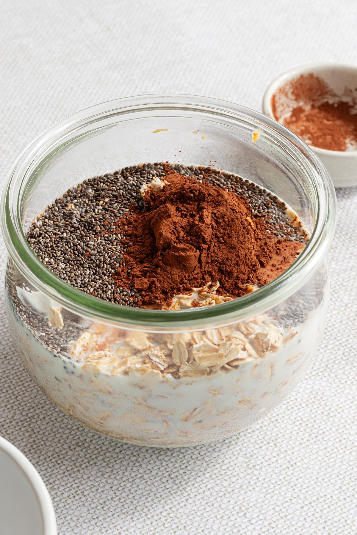 A jar full of oats, chia seeds, yogurt, milk, cocoa powder, maple syrup, and peanut butter.