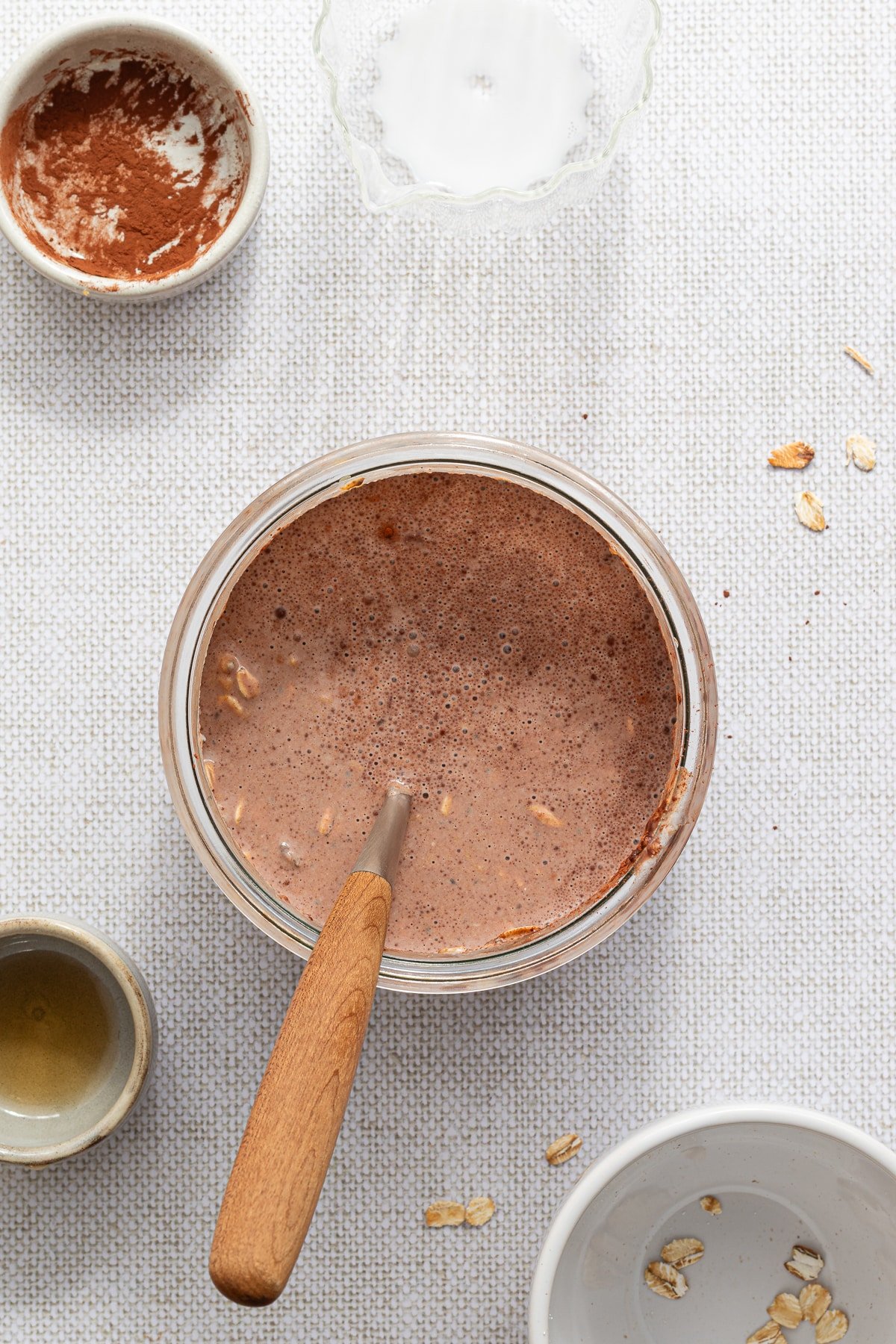 Mixing together oats, chia seeds, yogurt, milk, cocoa powder, maple syrup, and peanut butter in a jar.
