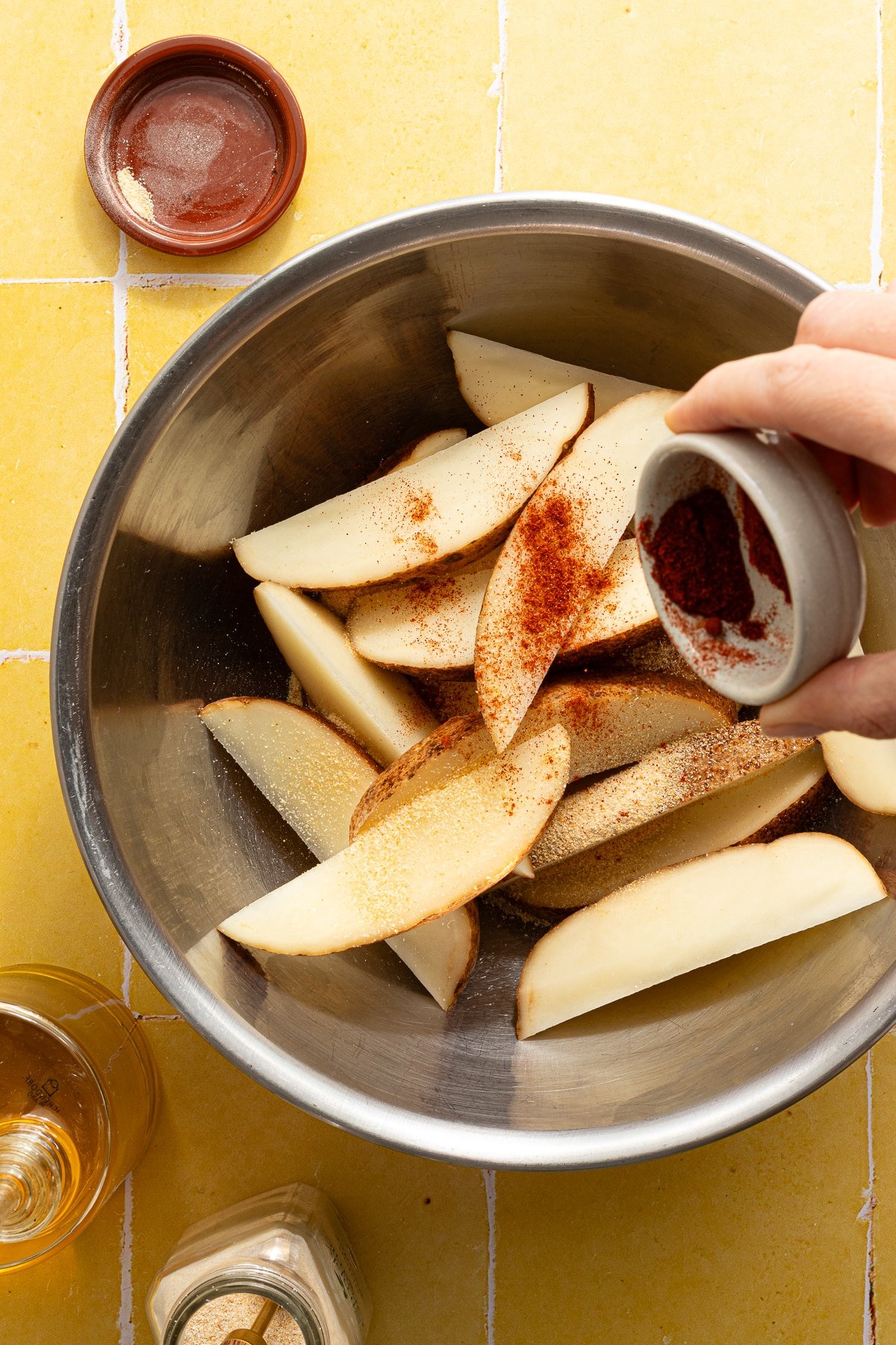 Seasoning potato wedges with paprika.