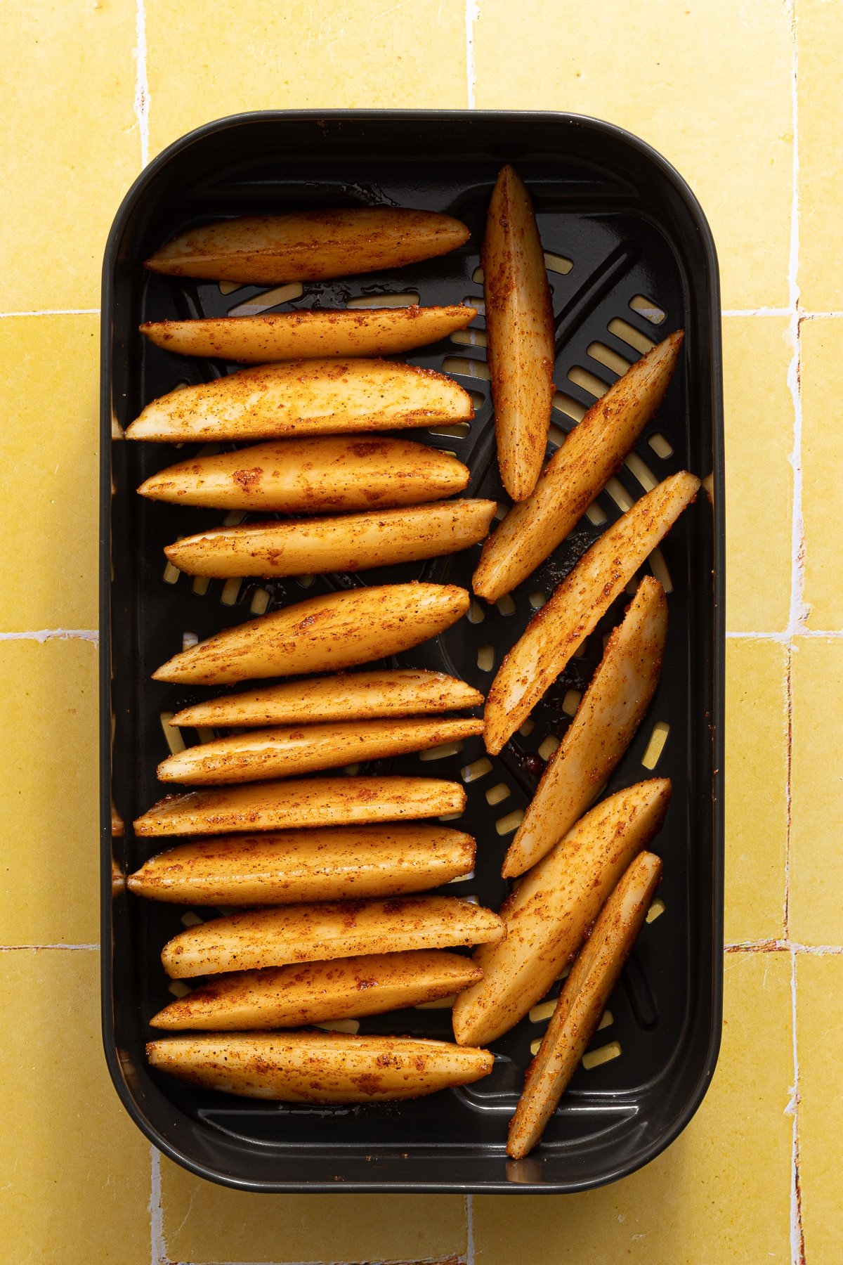 Seasoned potato wedges in the basket of an air fryer.